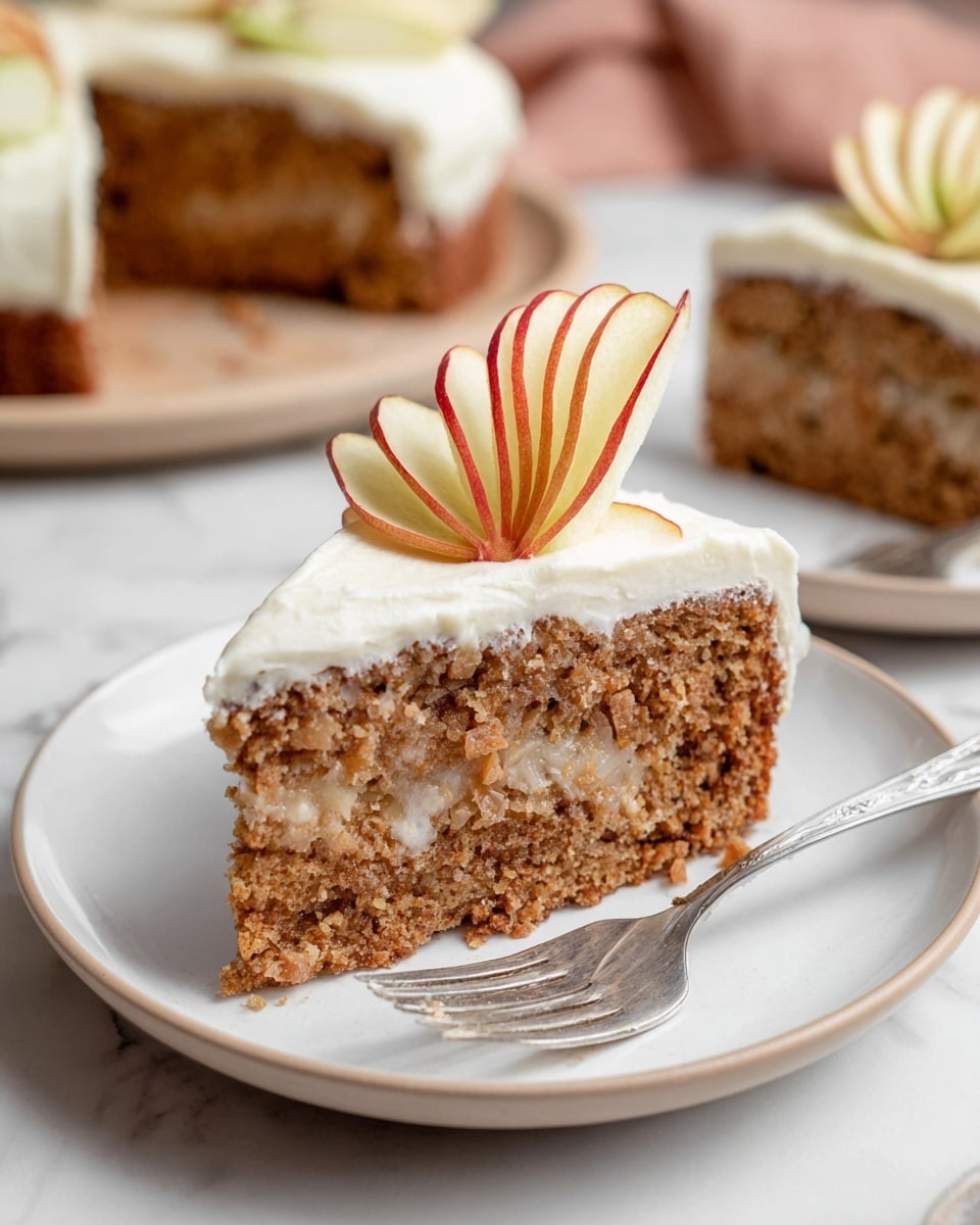 A slice of moist, brown cake with visible small chunks inside forms the bottom layer, topped by a smooth, thick, creamy white frosting layer. On top of the frosting, a single, thin, ruffled dried apple slice with a red edge decorates the cake. The slice sits on a white plate with a fork beside it, all placed on a white marbled surface. In the background, more slices of the same cake are partially visible on white plates. Photo taken with an iphone --ar 4:5 --v 7