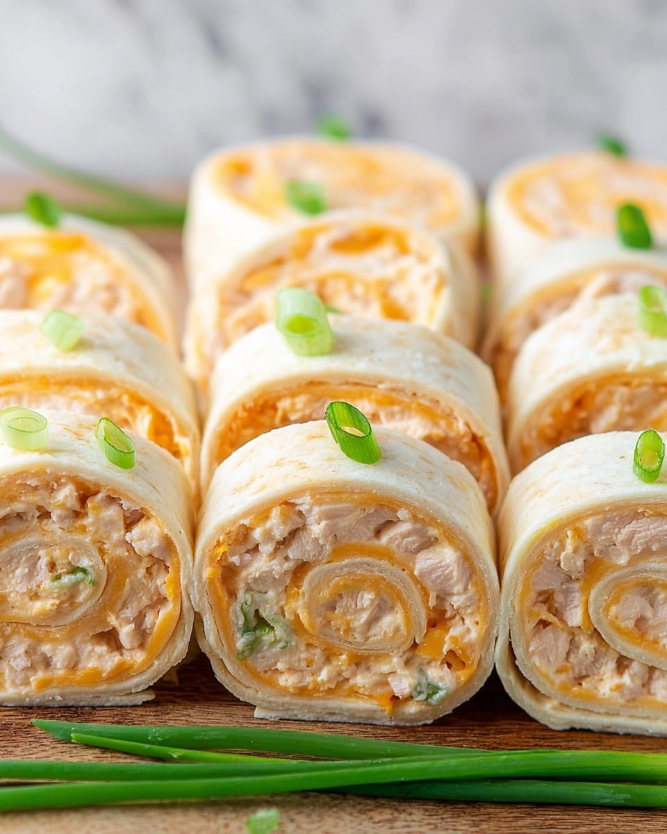 The image shows several close-up pinwheel rolls arranged in neat rows, each consisting of three visible layers: a soft, pale tortilla wrap on the outside, a middle layer of light cream cheese or similar spread mixed with small chunks of pale chicken, and an inner layer of orange shredded cheese. The pinwheels are tightly rolled to show the swirled pattern of these layers, with small green onion slices scattered around them as garnish. The rolls sit on a wooden surface against a white marbled texture background. photo taken with an iphone --ar 4:5 --v 7
