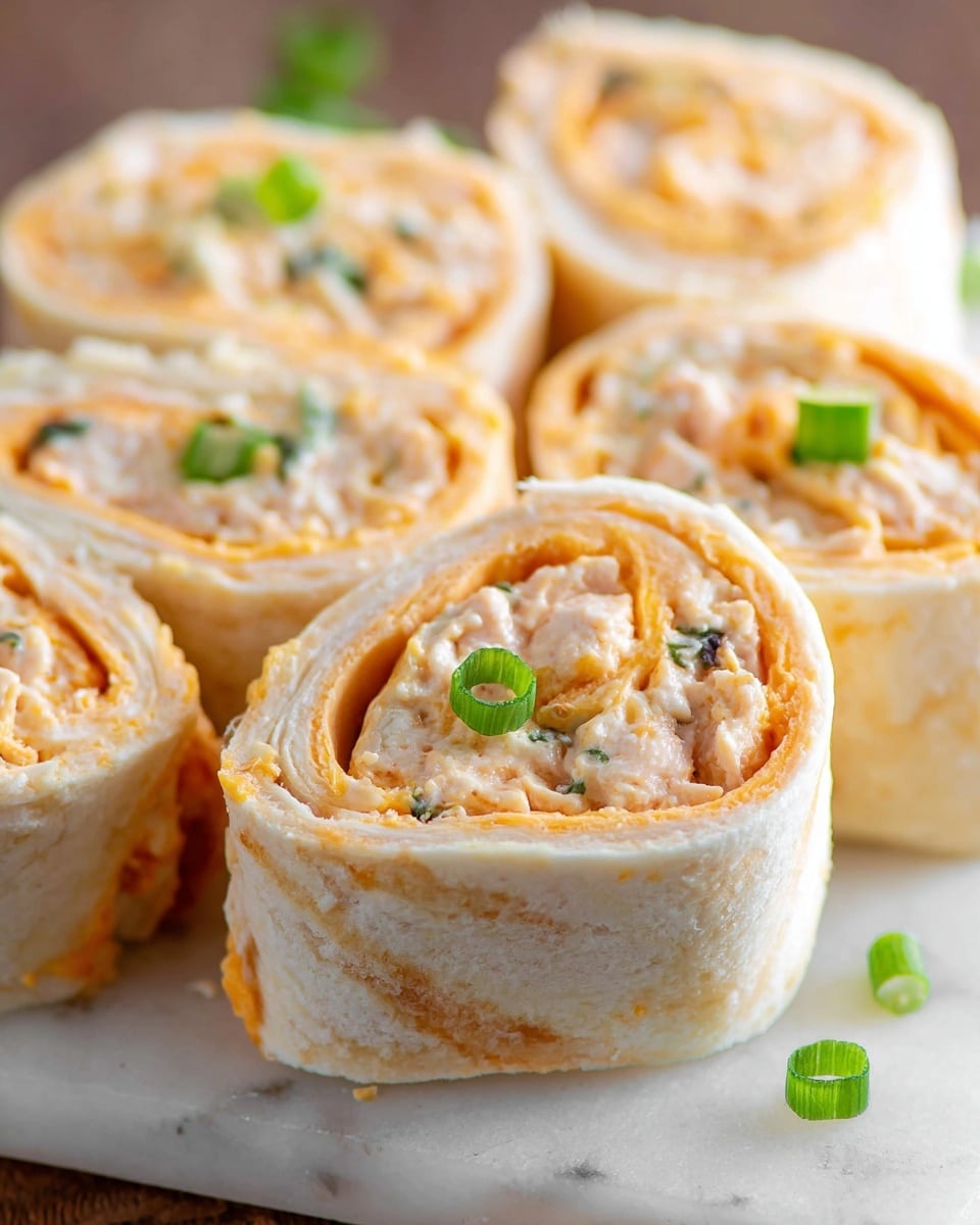 The image shows several rolled pinwheel sandwiches placed closely together on a white marbled surface. Each roll features three main layers: a soft, white tortilla wrapping around a filling that includes a light orange spread mixed with white and small dark bits, likely cheese and chicken or tuna salad. The interior has a swirled pattern created by the rolled layers. On top of each pinwheel is a small slice of green onion for garnish. The texture looks creamy and soft with a slight firm outer tortilla layer. Photo taken with an iphone --ar 4:5 --v 7