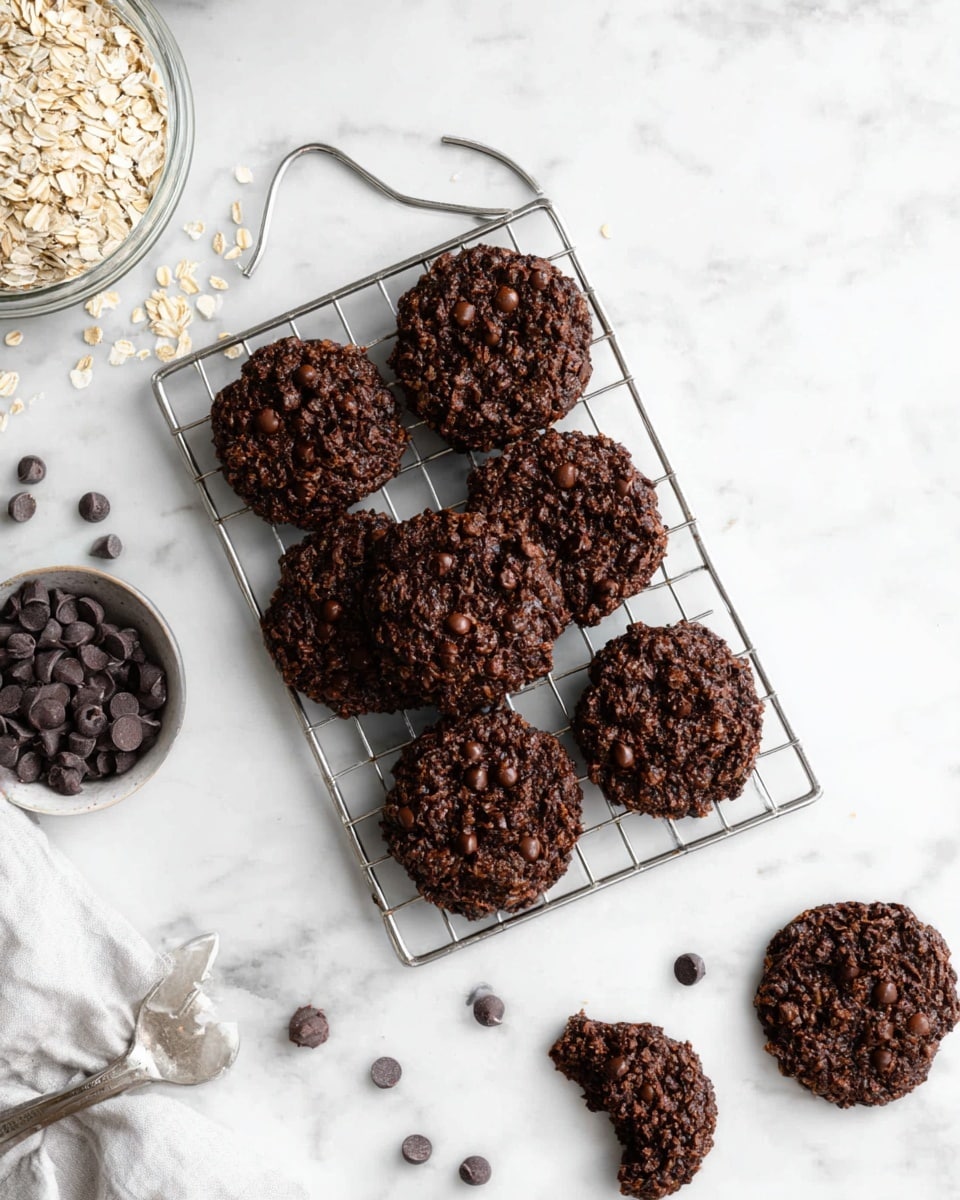 The image shows nine round dark chocolate cookies with visible chocolate chips and oats, arranged on a silver cooling rack with a handle, placed on a white marbled surface. One cookie is slightly overlapping another, and a single cookie is off to the side, broken into pieces. There are bowls around the rack with light-colored oats and dark chocolate chips scattered nearby. The overall look is rustic and textured, with the cookies having a rough, chunky surface. photo taken with an iphone --ar 4:5 --v 7