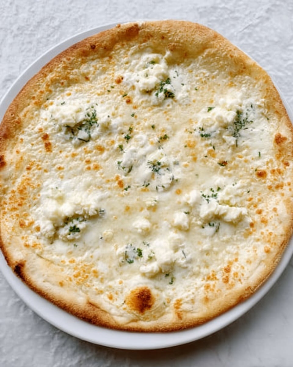 The image shows a round pizza with a thin, light golden crust on a white plate. The pizza has one layer of melted white cheese covering the whole top. On top of the cheese, there are small, irregularly shaped pieces of pale white cheese spread evenly. Small patches of green herbs can be seen scattered lightly across the surface. The pizza rests on a white marbled surface. photo taken with an iphone --ar 4:5 --v 7