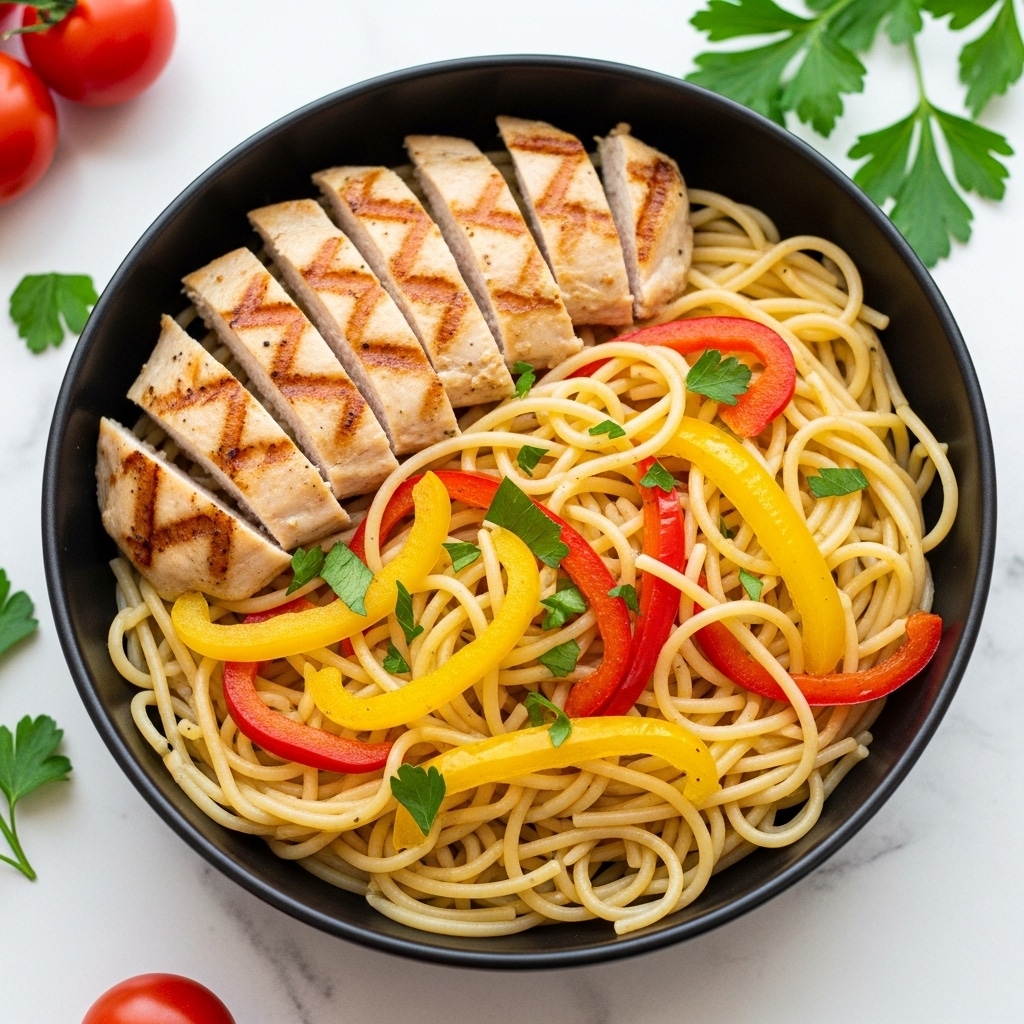The image shows a black bowl filled with a layer of light yellow spaghetti at the bottom, topped with pieces of grilled chicken that are light brown with grill marks. Mixed throughout the pasta are thin, colorful strips of red and yellow bell peppers adding bright red and yellow accents. Small green parsley pieces are sprinkled on top for a fresh look. The bowl sits on a white marbled surface with some tomatoes and green herbs around it. photo taken with an iphone --ar 4:5 --v 7